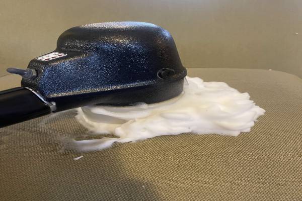 An upholstery cleaning device rubbing cleaning foam onto a couch